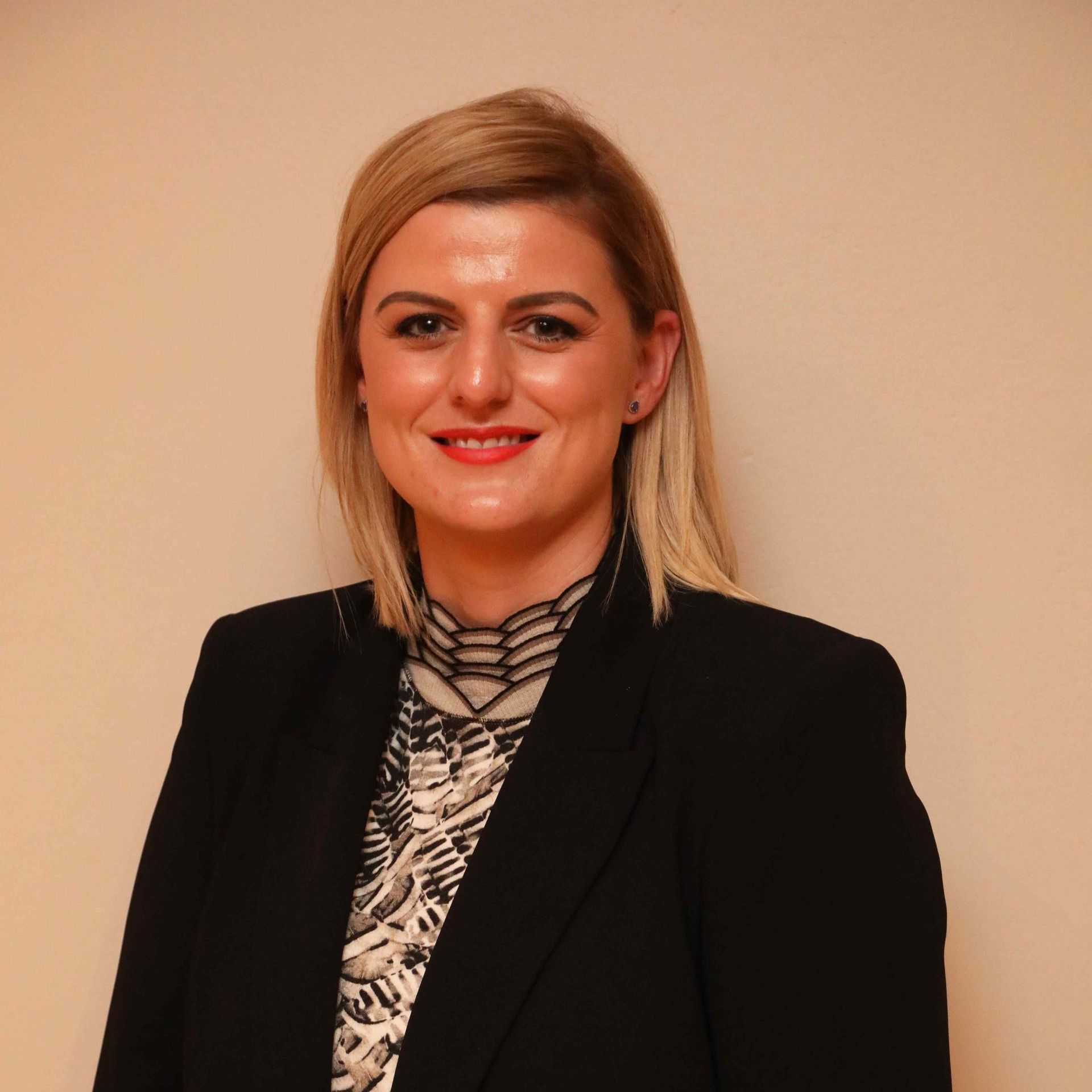 Portrait of a smiling person in a black blazer against a beige background