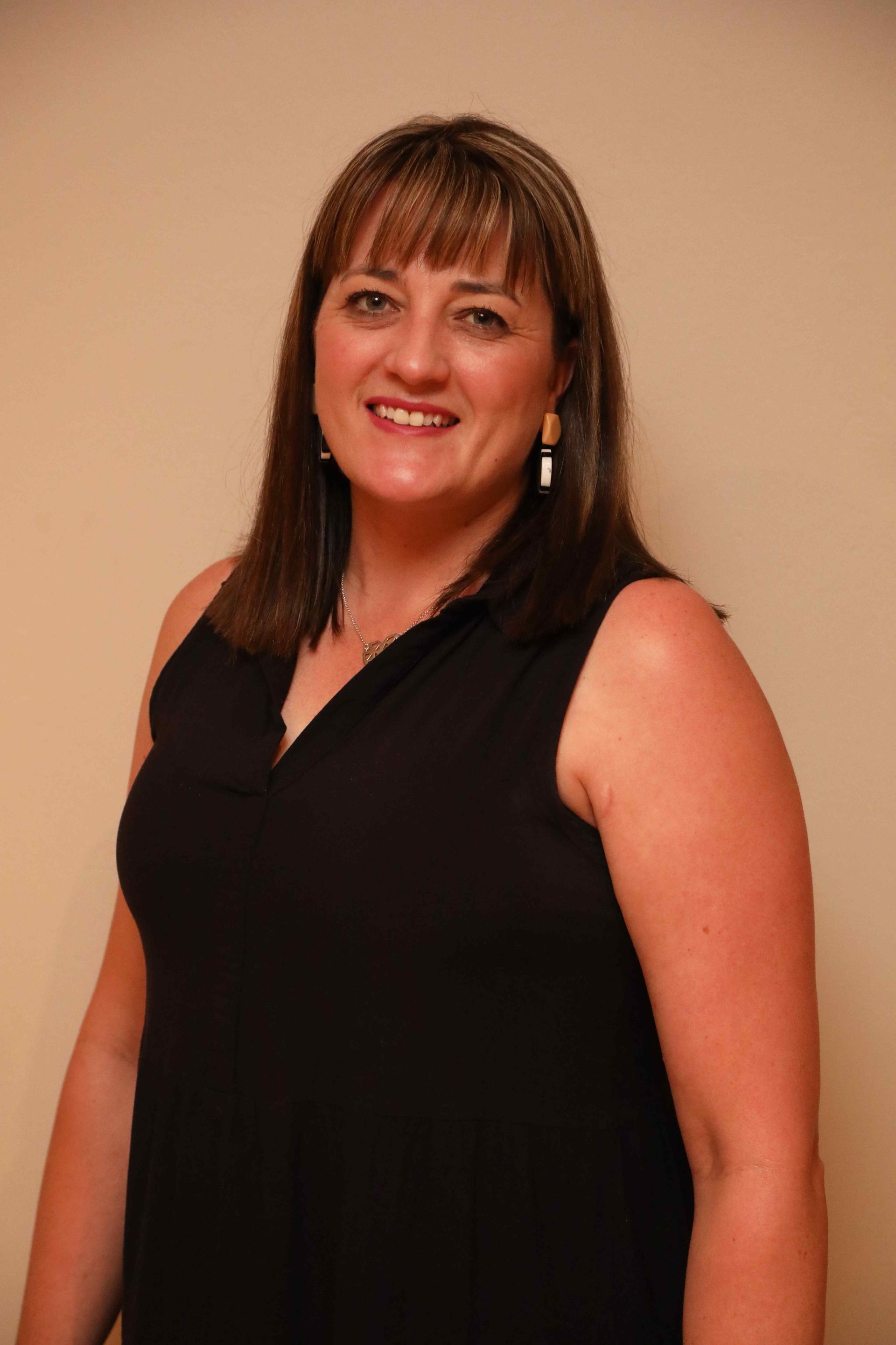 Woman in a black sleeveless top smiling against a plain tan background