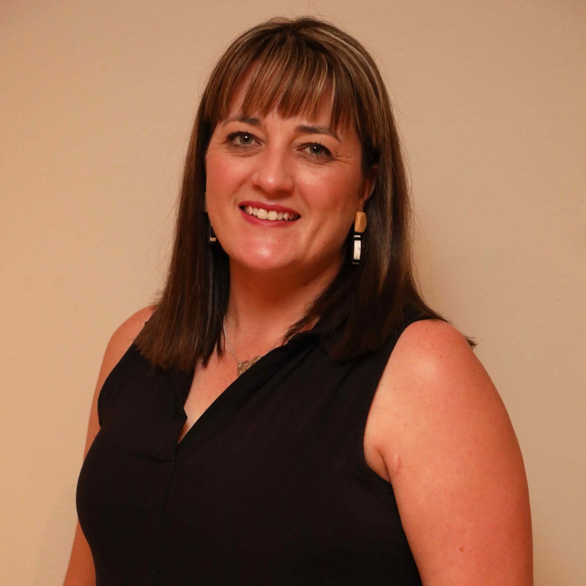 Smiling woman in a sleeveless black top against a beige wall.