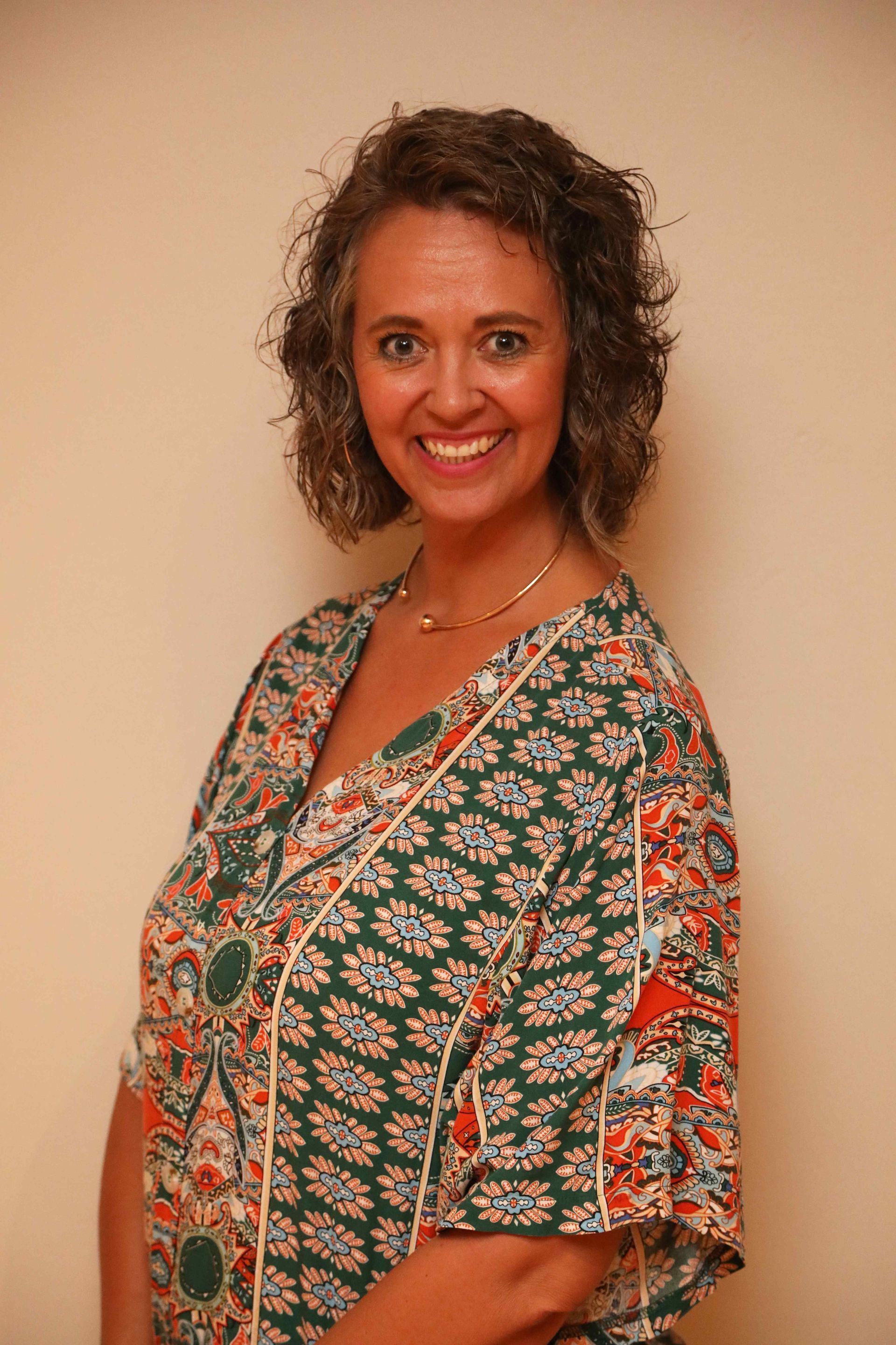 Woman in a patterned green dress smiling against a plain beige wall