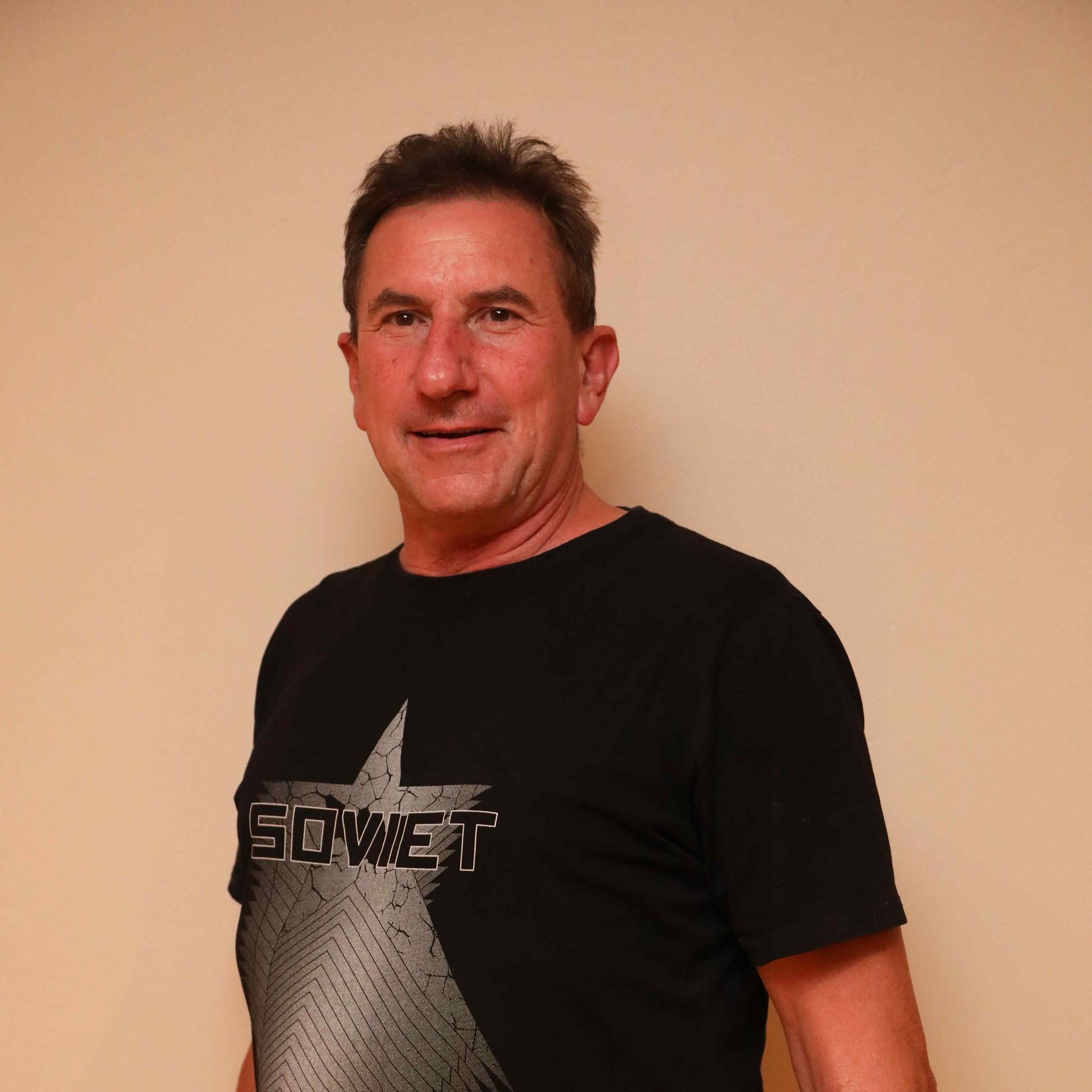 Man in a black graphic T-shirt standing against a beige wall