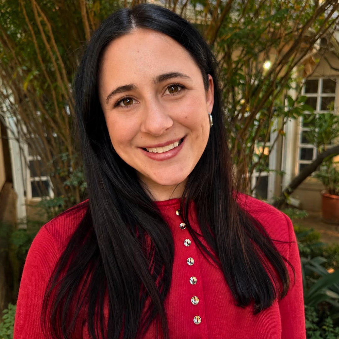 Smiling person in a red buttoned top outdoors with trees in the background
