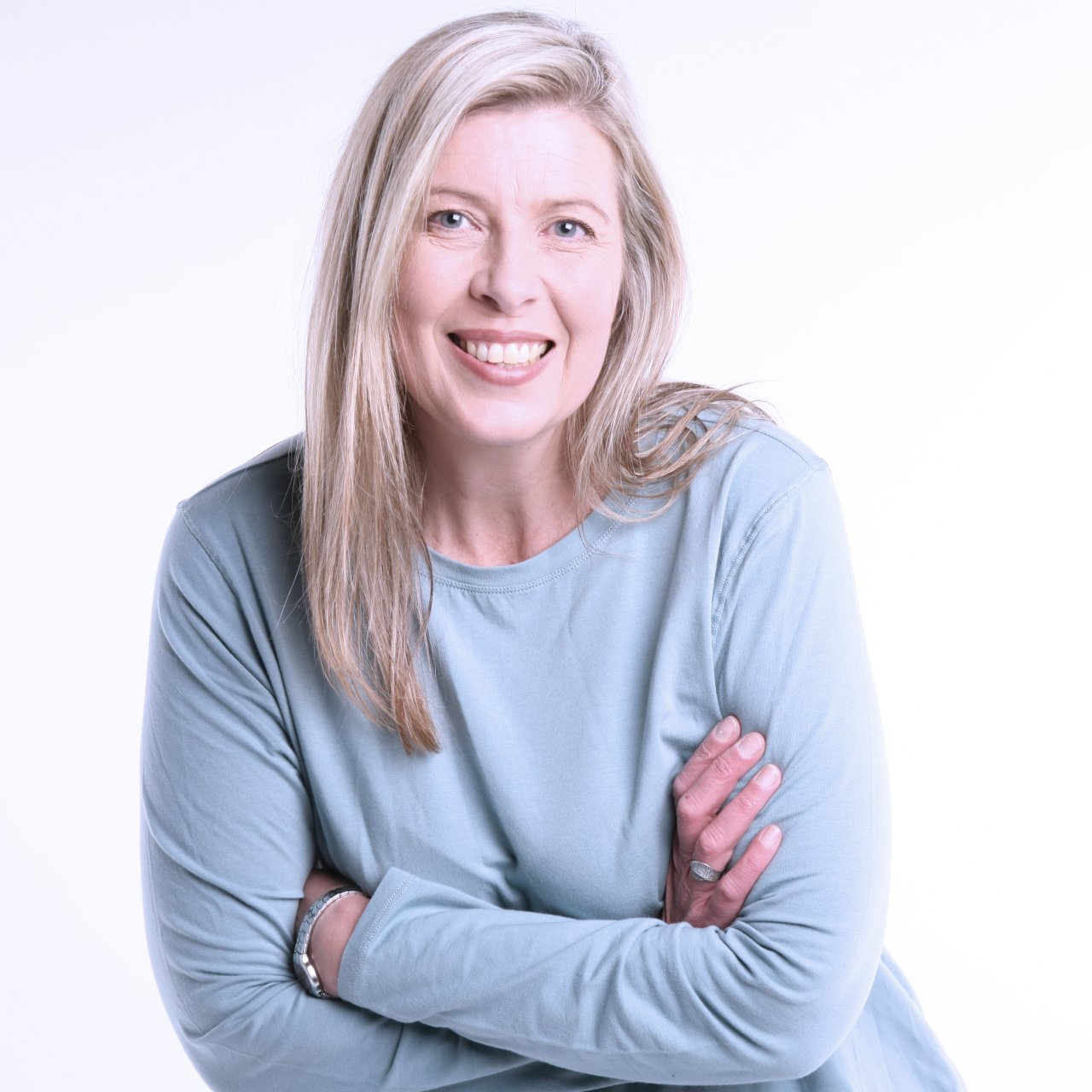 Smiling woman in a light blue sweater with arms crossed against a white background