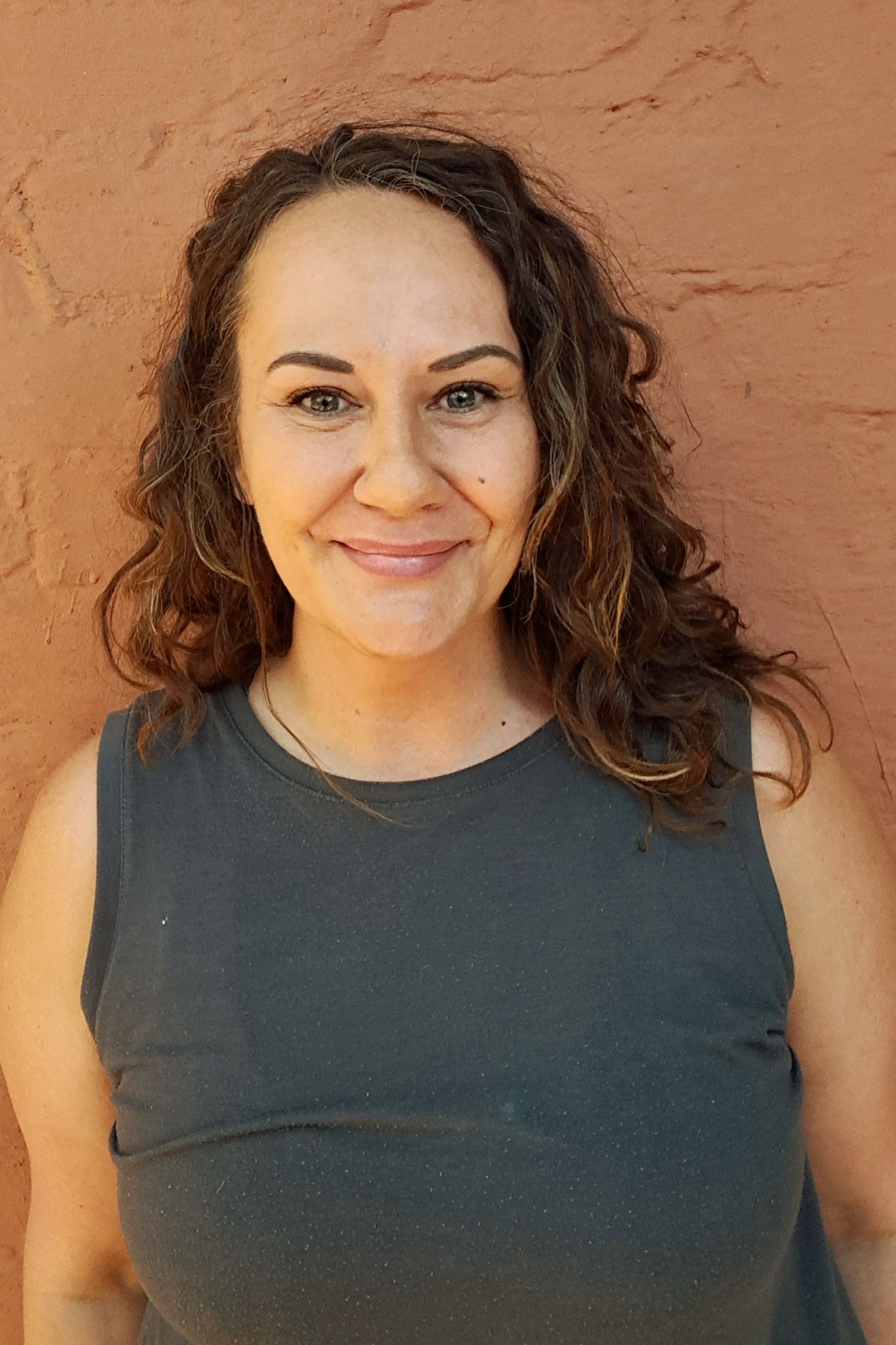 Woman smiling in a dark sleeveless shirt against a terracotta wall.