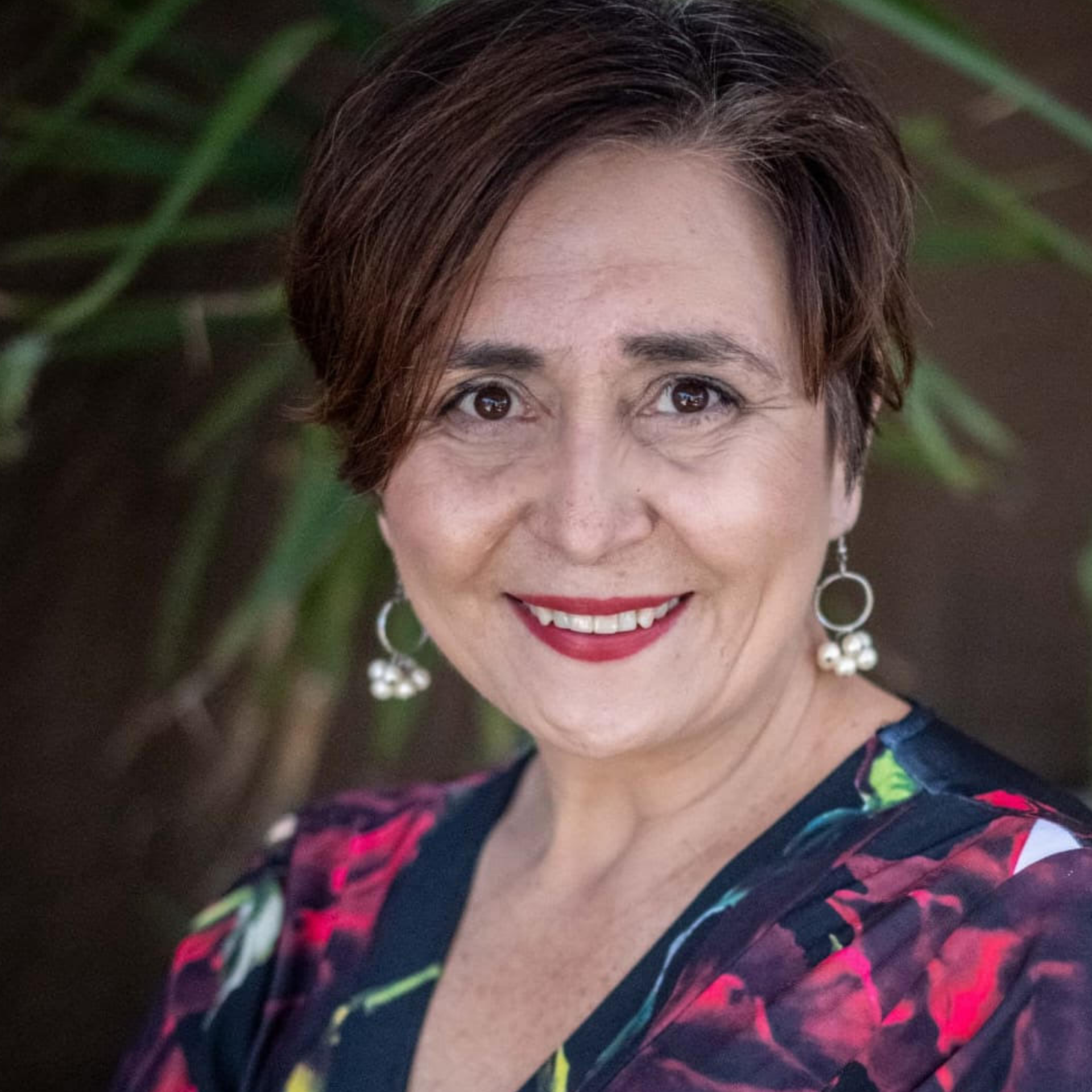 Smiling woman in floral blouse and dangling earrings against a blurred green background