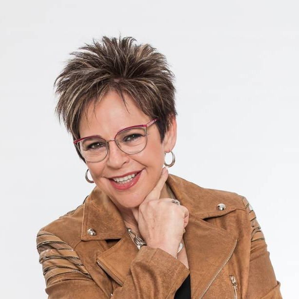 Smiling person in glasses and tan jacket against a light background