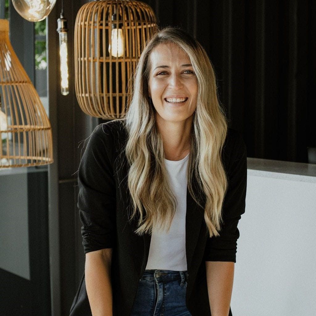 Smiling woman in a black cardigan and white shirt standing in a modern café interior