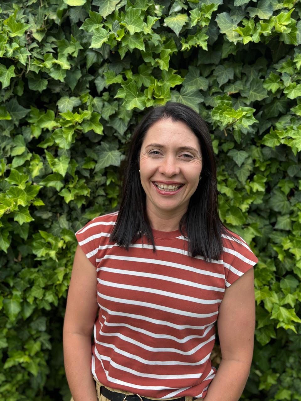 Smiling woman in a red-and-white striped shirt standing before a green ivy wall