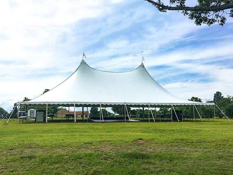 Large white event tent on a grassy field under a blue sky with clouds