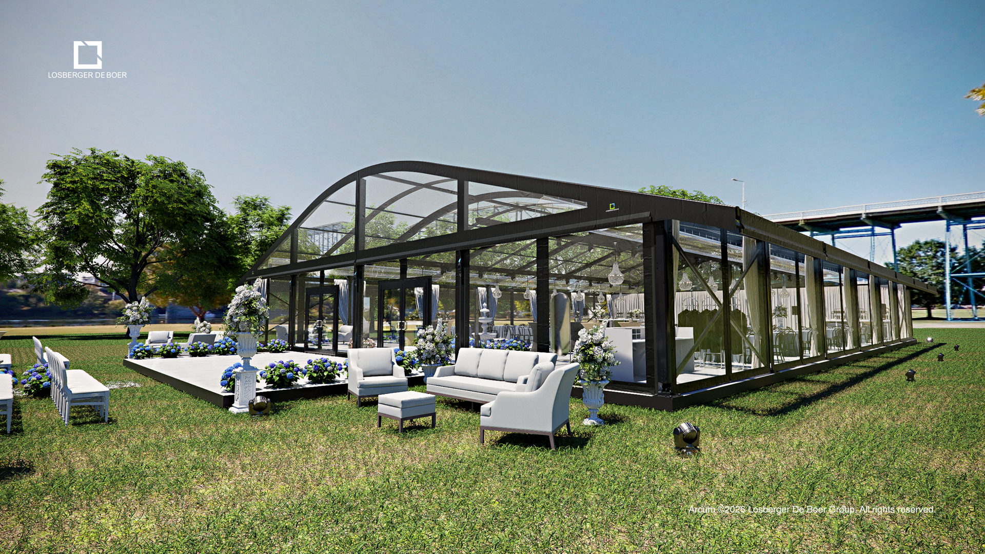 Outdoor lounge with white sofas and chairs beside a glass pavilion on a sunny grassy lawn.