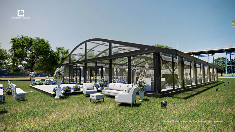 Outdoor lounge with white chairs and tables beside a modern glass pavilion on a grassy lawn under a blue sky