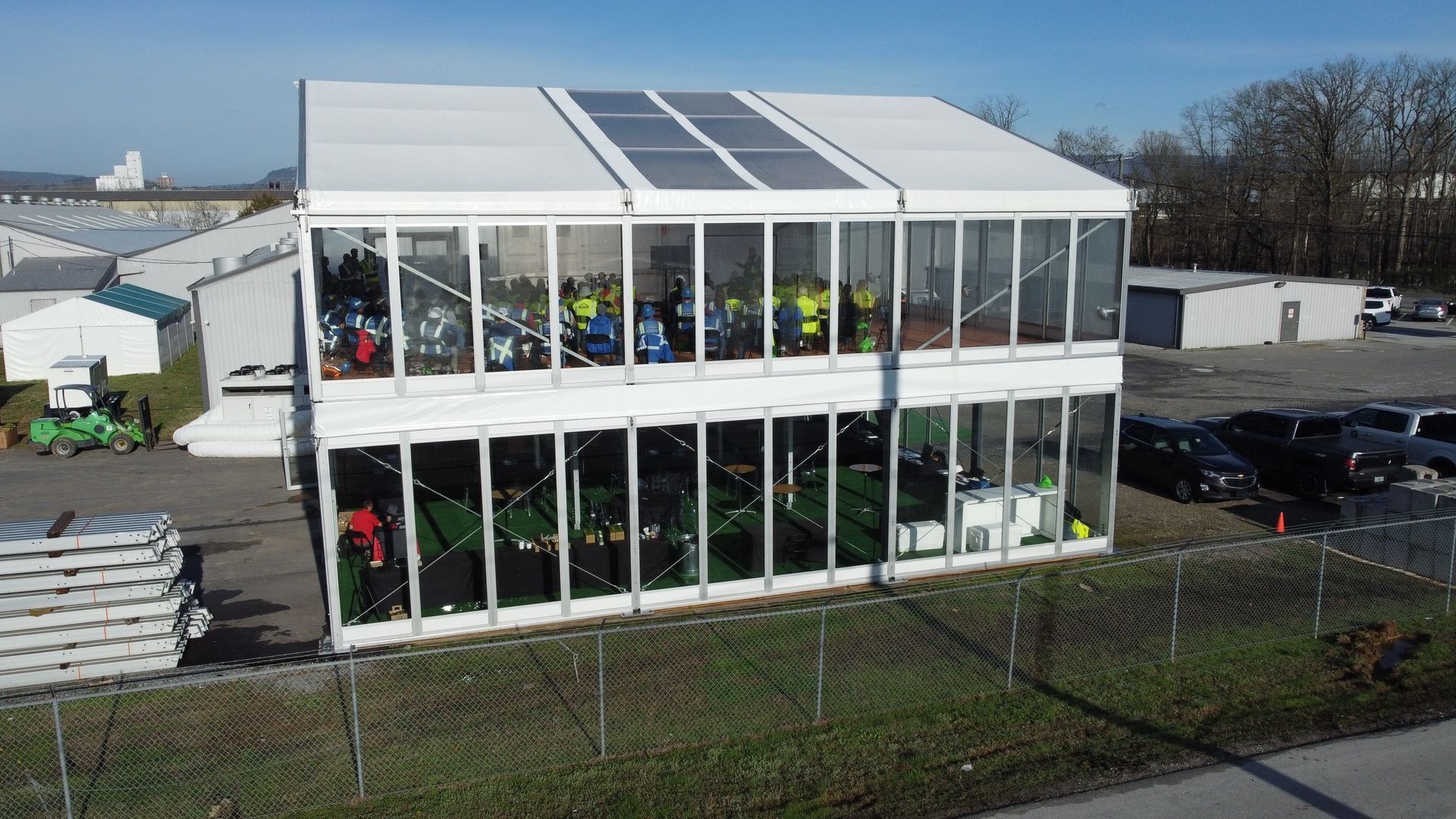 Large white two-story glass building with people inside, viewed from outside on a sunny day.