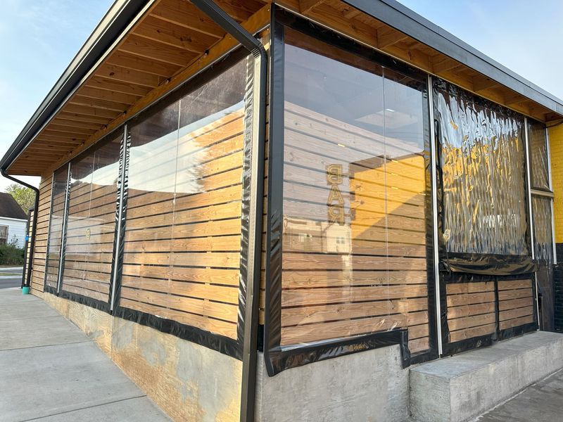 Modern wooden building with large windows and black framing on a concrete walkway