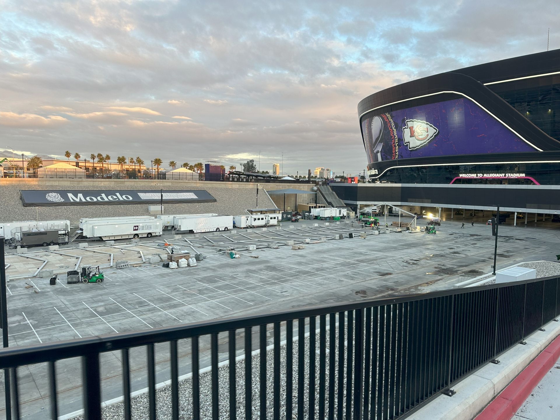 Snowy outdoor arena at dusk with a purple-lit stadium, covered field, and cloudy sky.