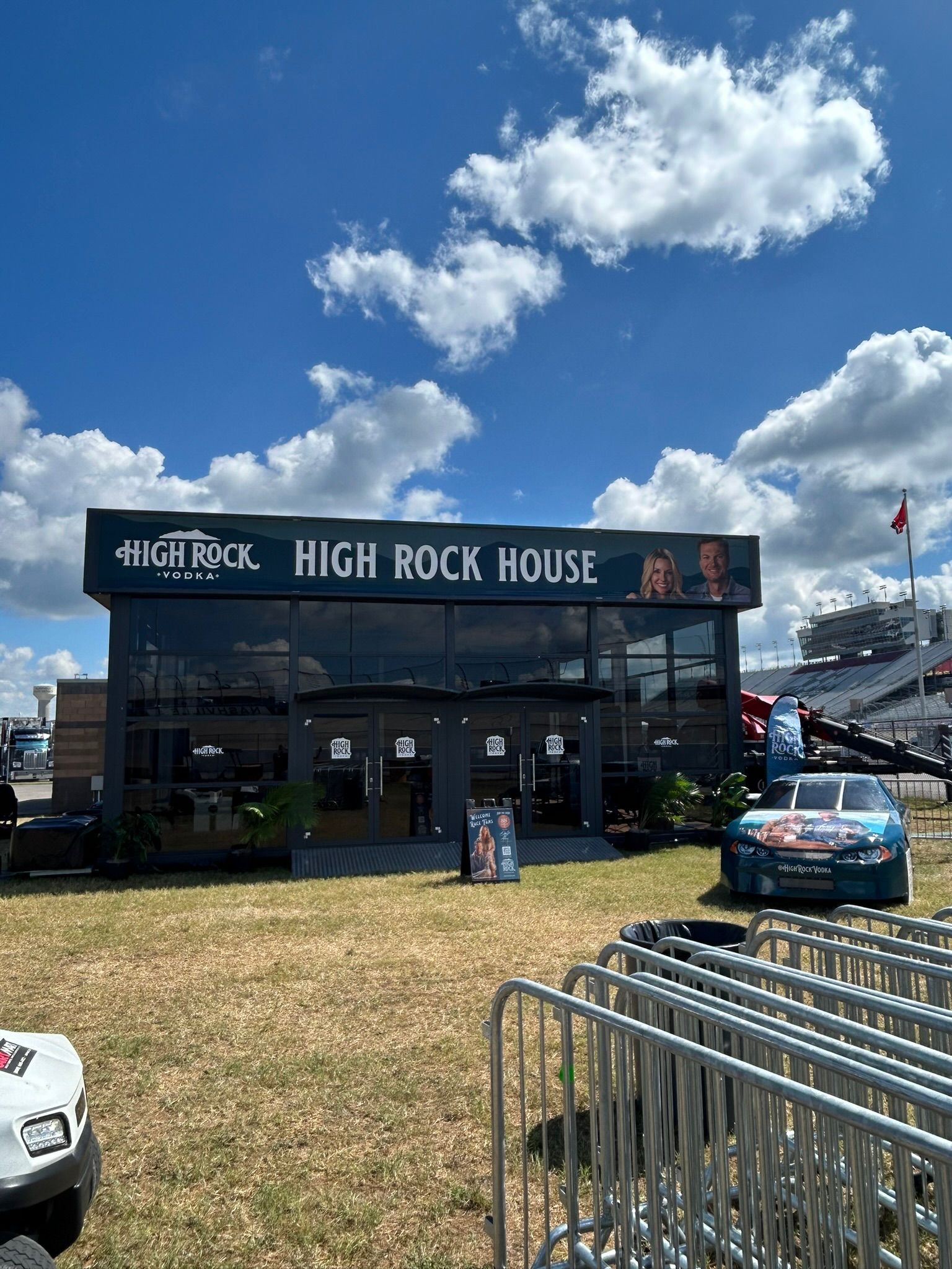 High Rock House tent at an outdoor event under a blue sky, with parked cars and metal barriers nearby