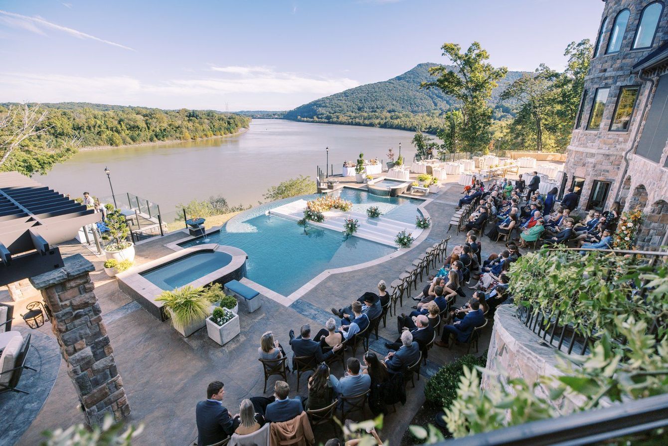 Lakeside poolside event with seated crowd, mountain view, and sunset over the water