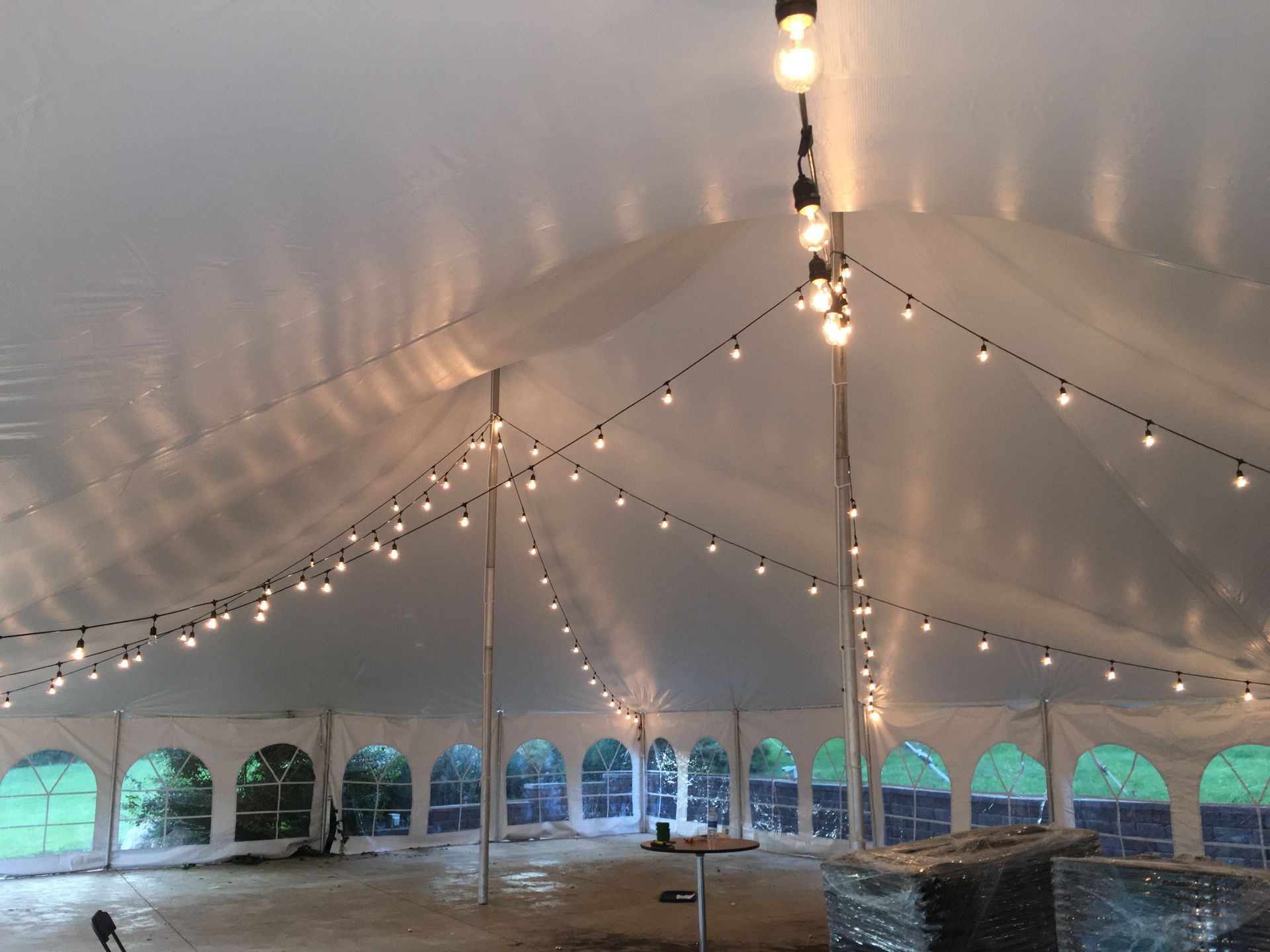Inside a white event tent, strings of warm lights hang from the ceiling over empty tables.
