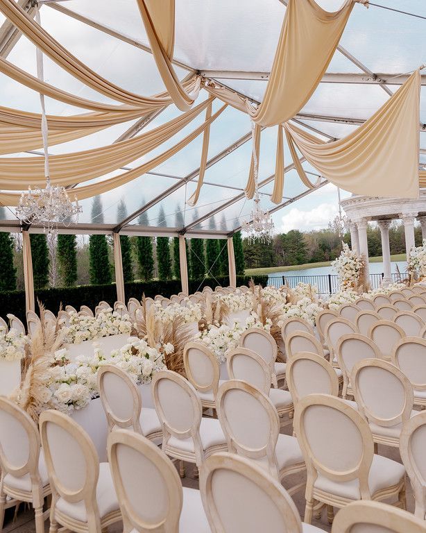 People socializing under a clear tent by a lake, with colorful rugs and tables set for an outdoor event