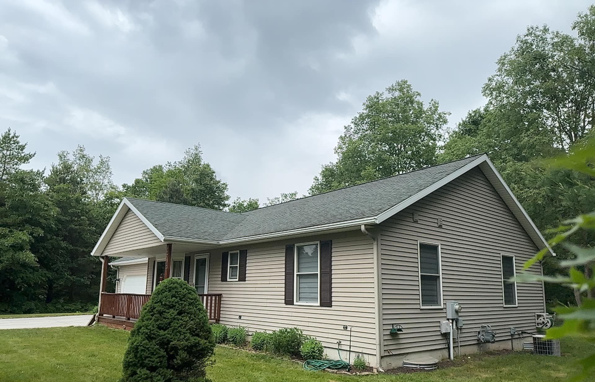 Single-story beige house with gray roof and striped siding in a green yard under cloudy sky