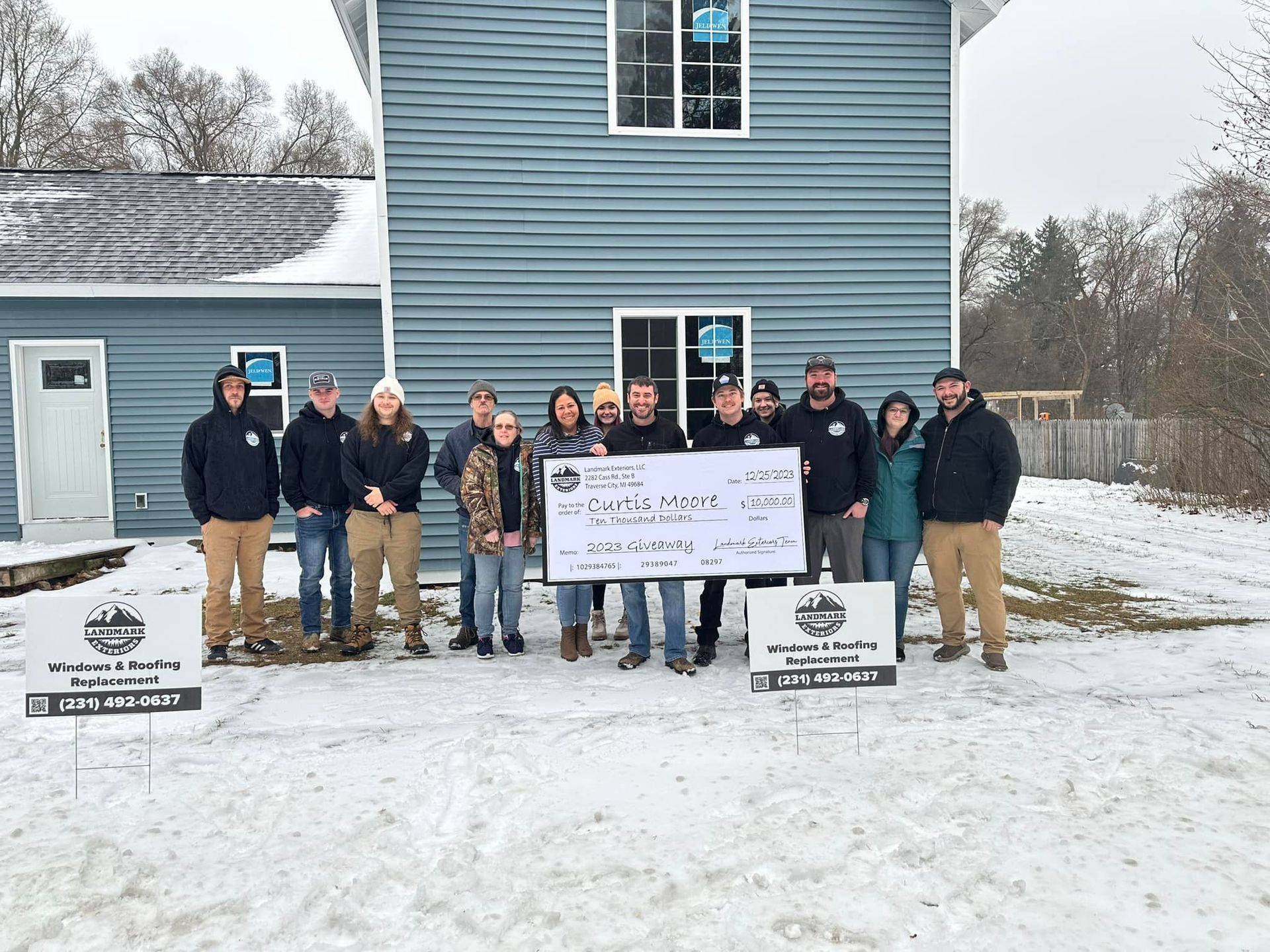 Group posing outdoors in winter holding a large sign in front of a blue building.
