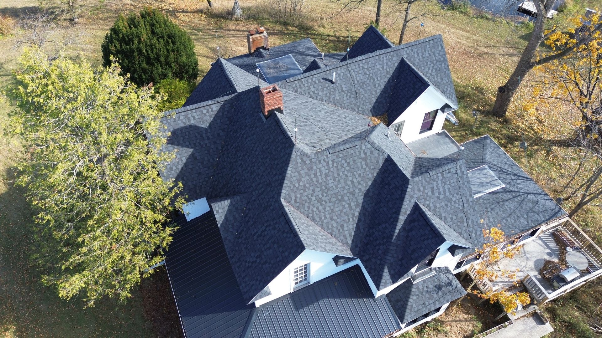 Aerial view of a dark gray shingled house roof surrounded by trees in autumn.
