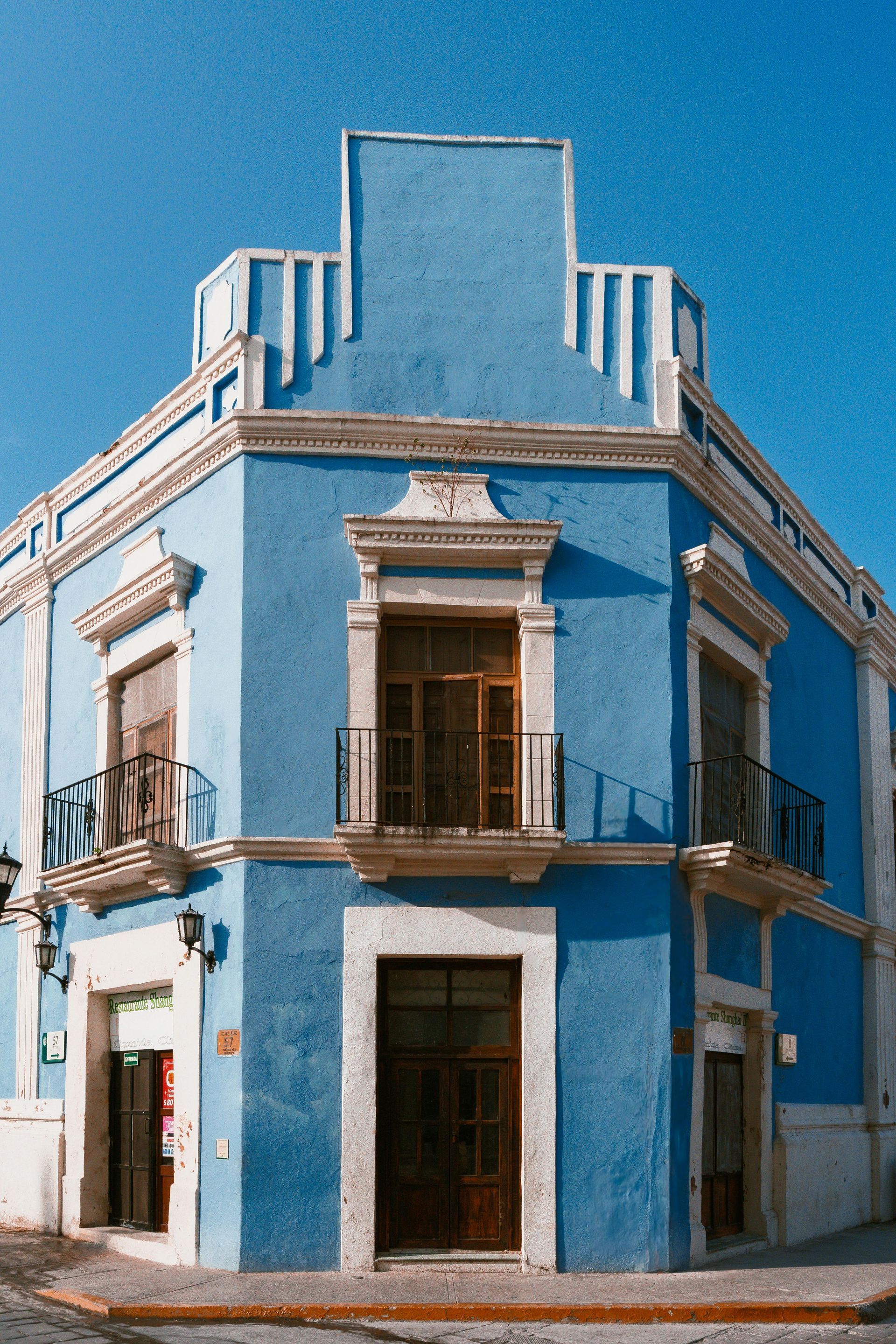 Blue corner building with ornate balconies and a wooden door against a clear sky