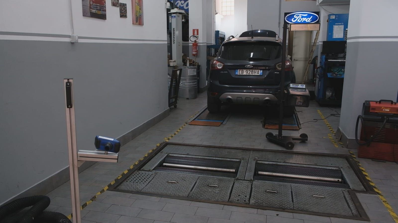 Un'auto nera su un ponte sollevatore in un'officina, con attrezzi e attrezzature visibili.