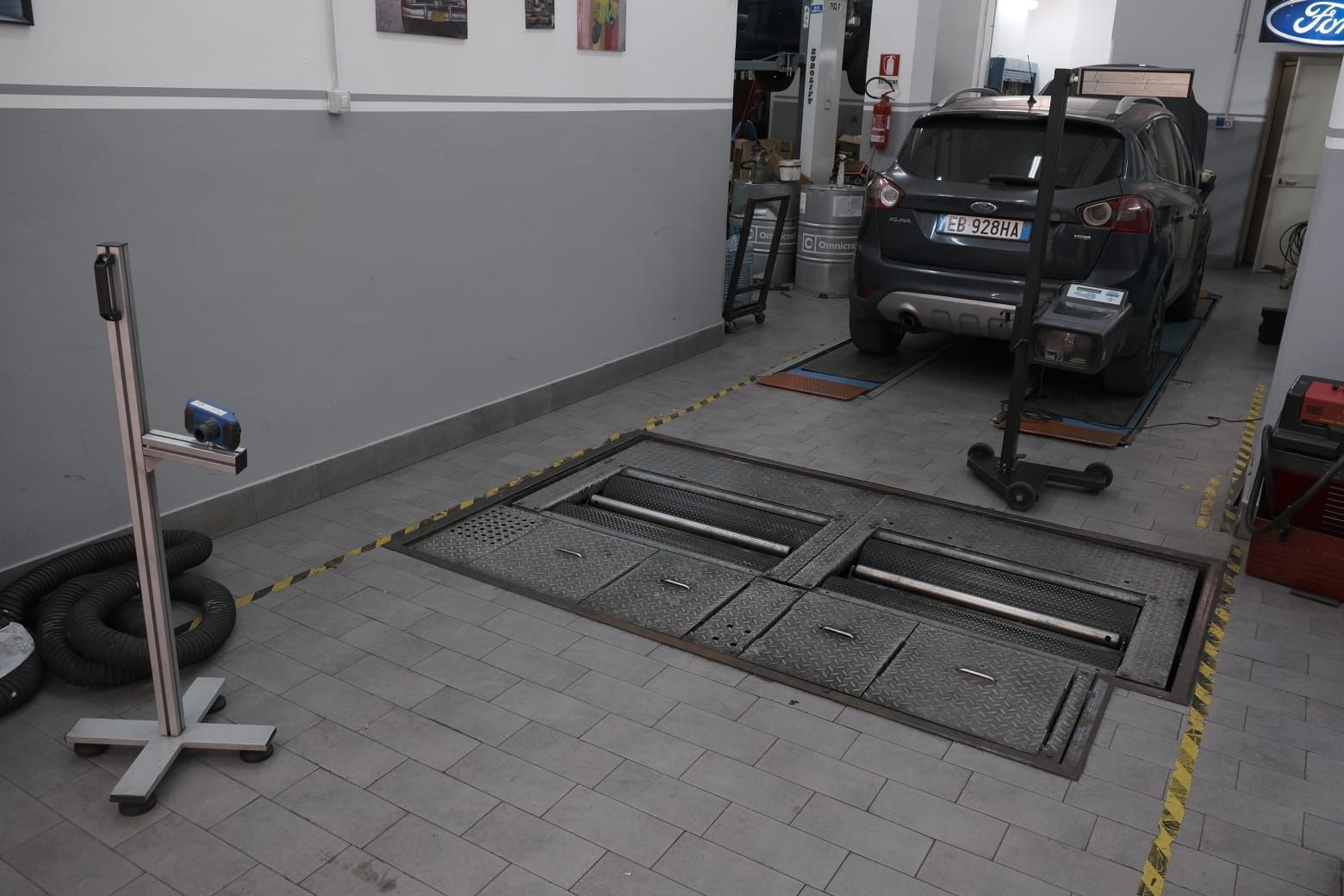 Auto in un garage, rivolta verso il retro. Pareti grigie, fossa a cielo aperto, attrezzatura di ispezione, veicolo nero, ambiente industriale.