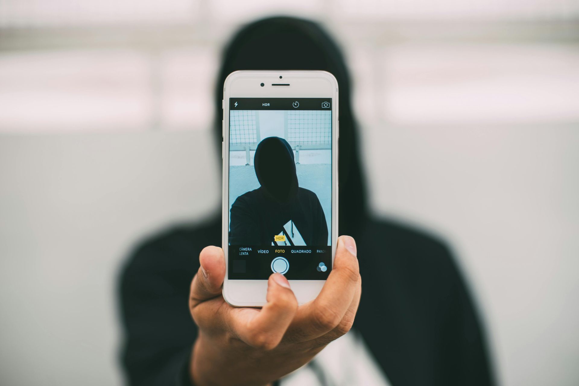 Person in black hooded jacket holding a phone, taking a selfie.