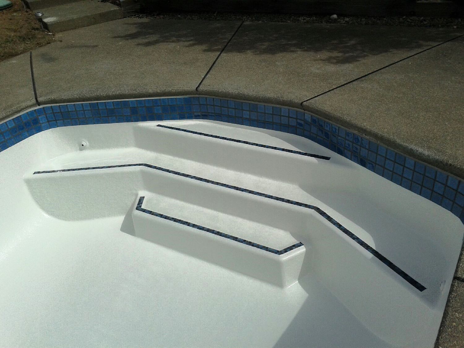 Pool steps painted white with dark handrails, blue tile trim, and gray concrete surround. Pool steps painted white with dark handrails, blue tile trim, and gray concrete surround.