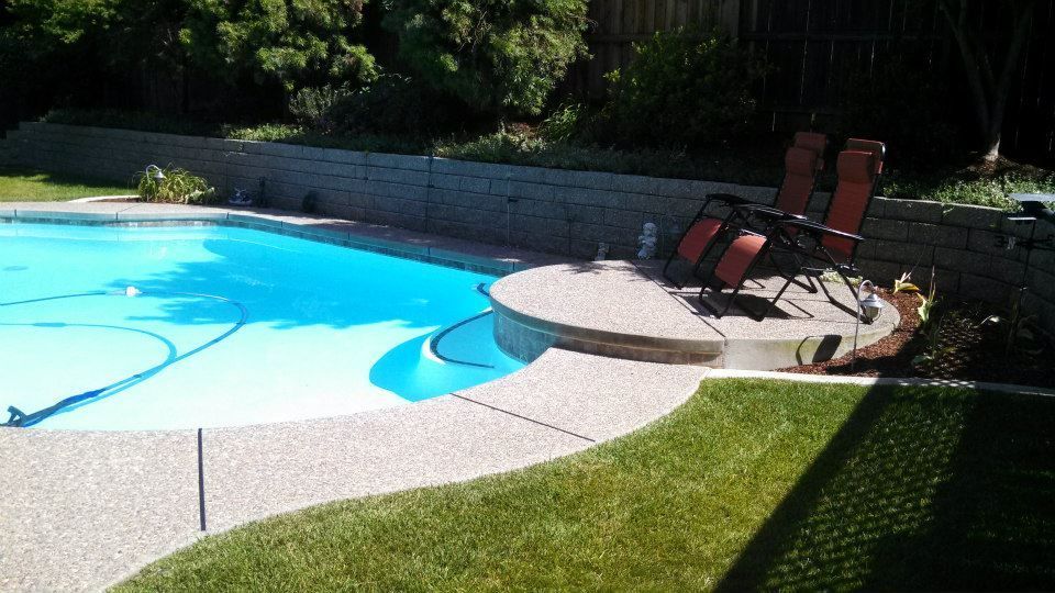 Poolside patio with lounge chairs, blue water, and green lawn.