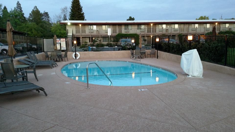 Pool area at a motel with lounge chairs, a covered hot tub, and the building in the background. Pool area at a motel with lounge chairs, a covered hot tub, and the building in the background.