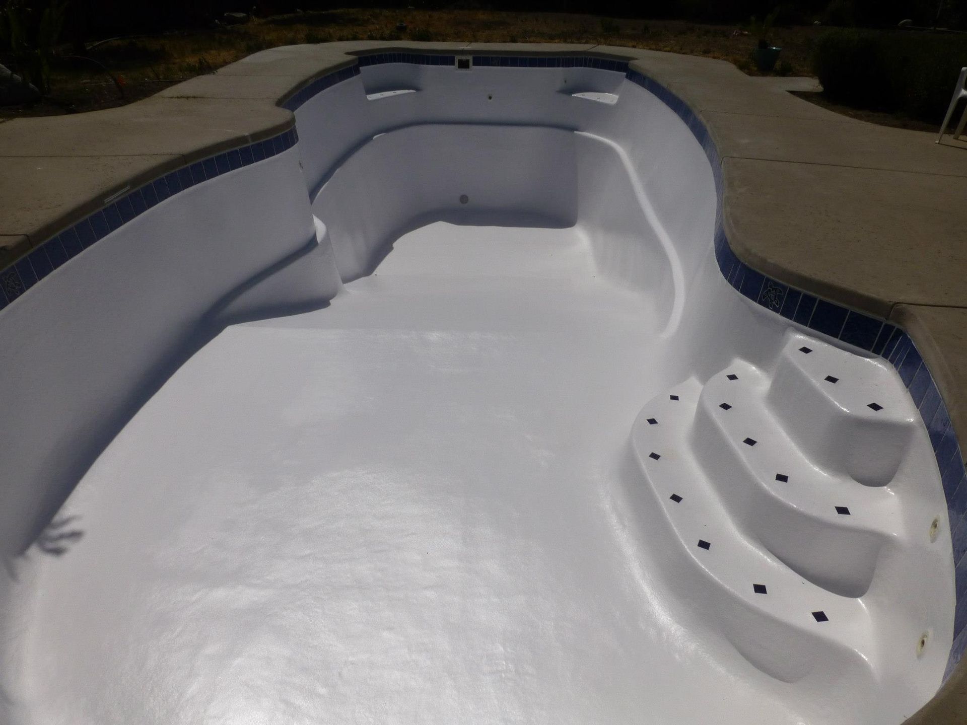 Empty swimming pool with white interior, blue tile border, and concrete surround. Empty swimming pool with white interior, blue tile border, and concrete surround.