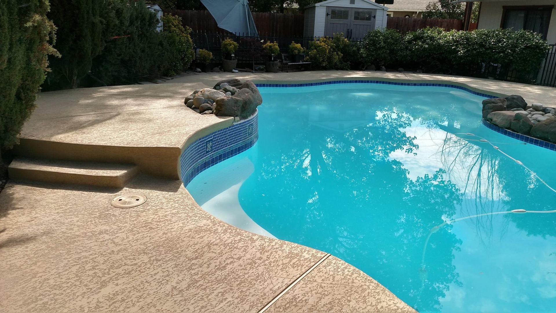 Pool with blue water and tan concrete surround; steps and rock accents.