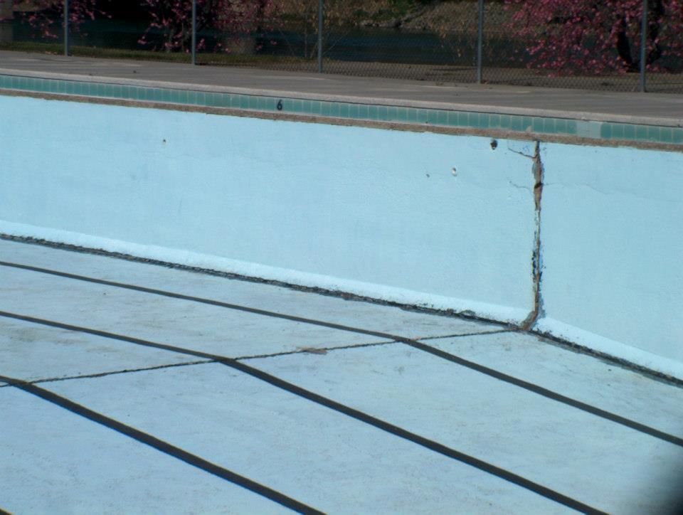 Empty, light-blue swimming pool with a large crack in the wall, sunlight casting shadows. Empty, light-blue swimming pool with a large crack in the wall, sunlight casting shadows.