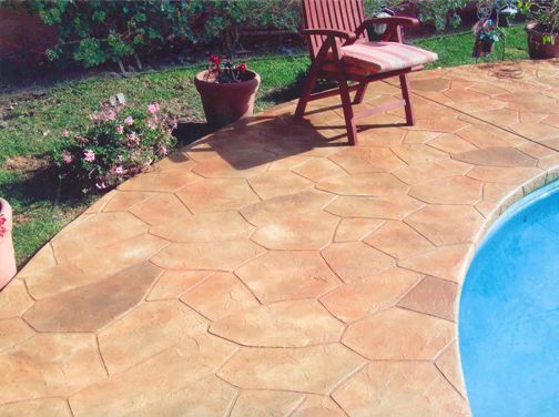 Stamped concrete patio with a stone pattern next to a pool and a chair.