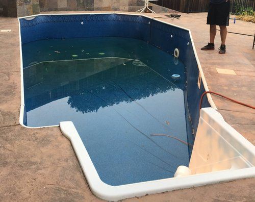 Empty blue pool with white coping, brown deck, and a person standing nearby. Empty blue pool with white coping, brown deck, and a person standing nearby.