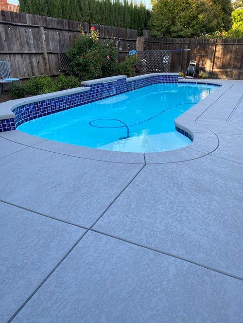 Swimming pool with blue water and tiled edge, surrounded by gray concrete patio and wooden fence. Swimming pool with blue water and tiled edge, surrounded by gray concrete patio and wooden fence.