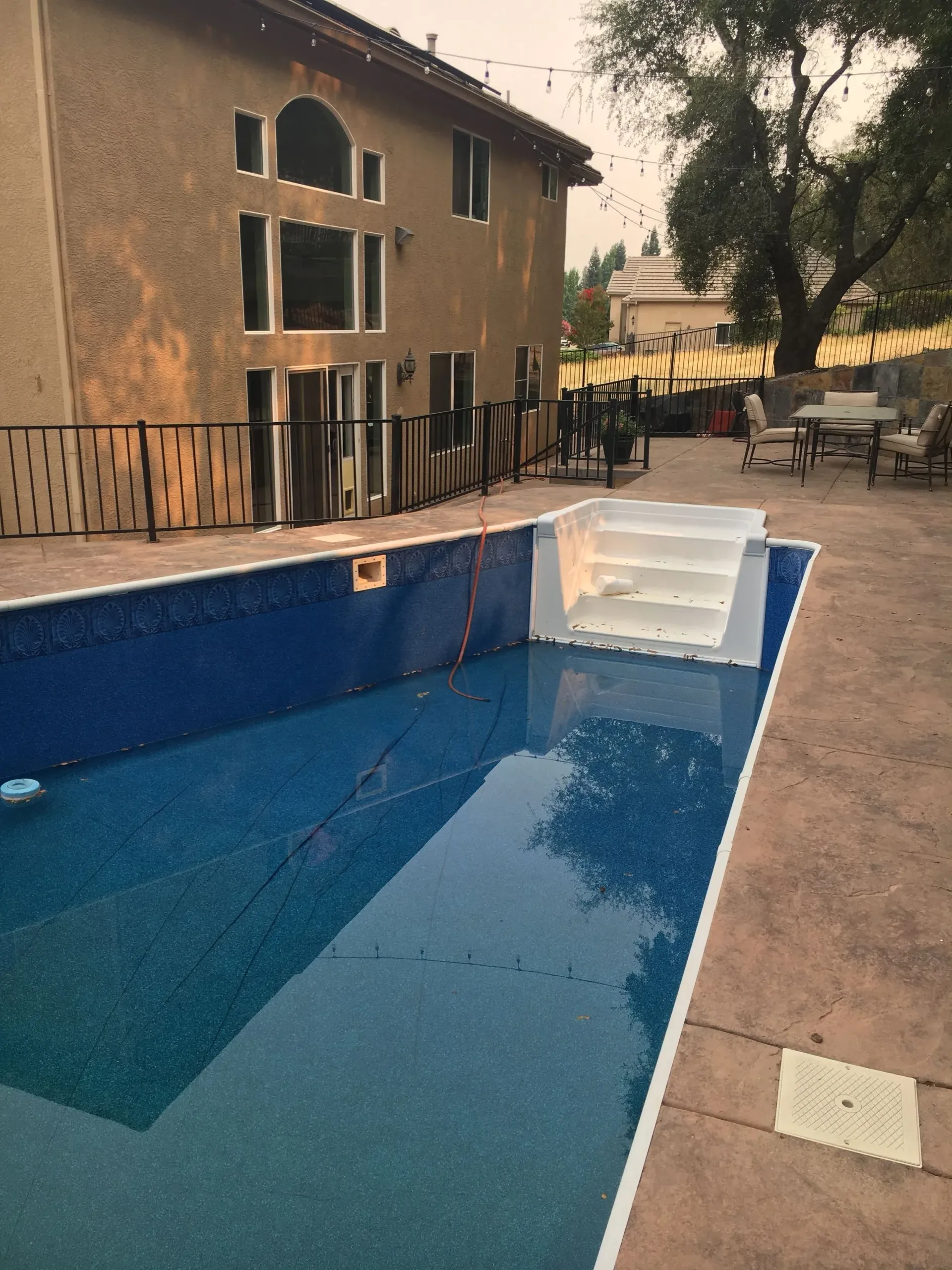 Backyard pool with blue tile interior next to a two-story beige house and patio furniture. Backyard pool with blue tile interior next to a two-story beige house and patio furniture.