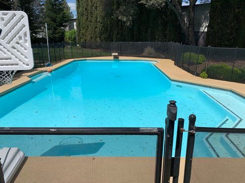 A turquoise swimming pool with a basketball hoop, surrounded by a black fence and concrete deck. A turquoise swimming pool with a basketball hoop, surrounded by a black fence and concrete deck.