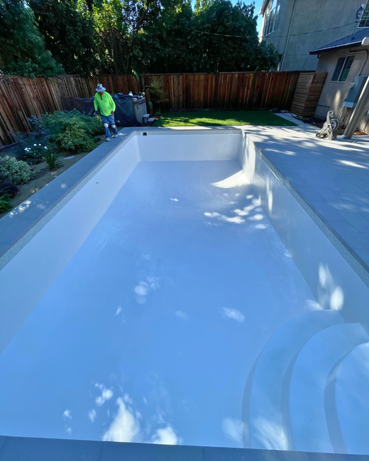 Backyard pool with blue tile interior next to a two-story beige house and patio furniture. Backyard pool with blue tile interior next to a two-story beige house and patio furniture.