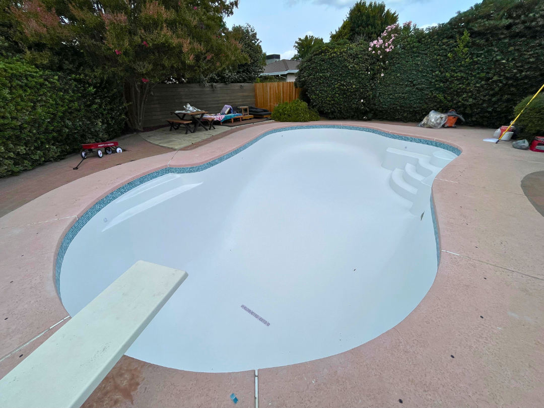 Backyard pool with blue tile interior next to a two-story beige house and patio furniture. Backyard pool with blue tile interior next to a two-story beige house and patio furniture.