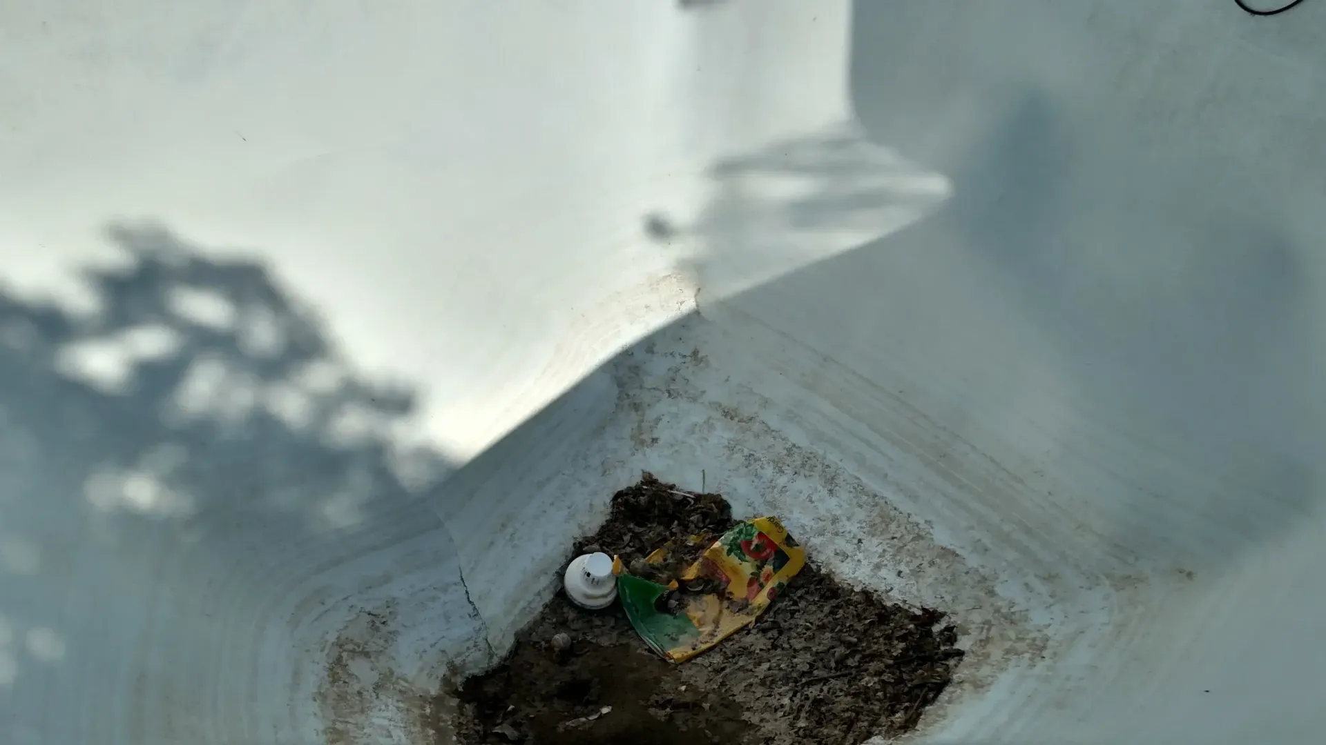 An overhead view of a white rectangular container with debris and shadows. An overhead view of a white rectangular container with debris and shadows.