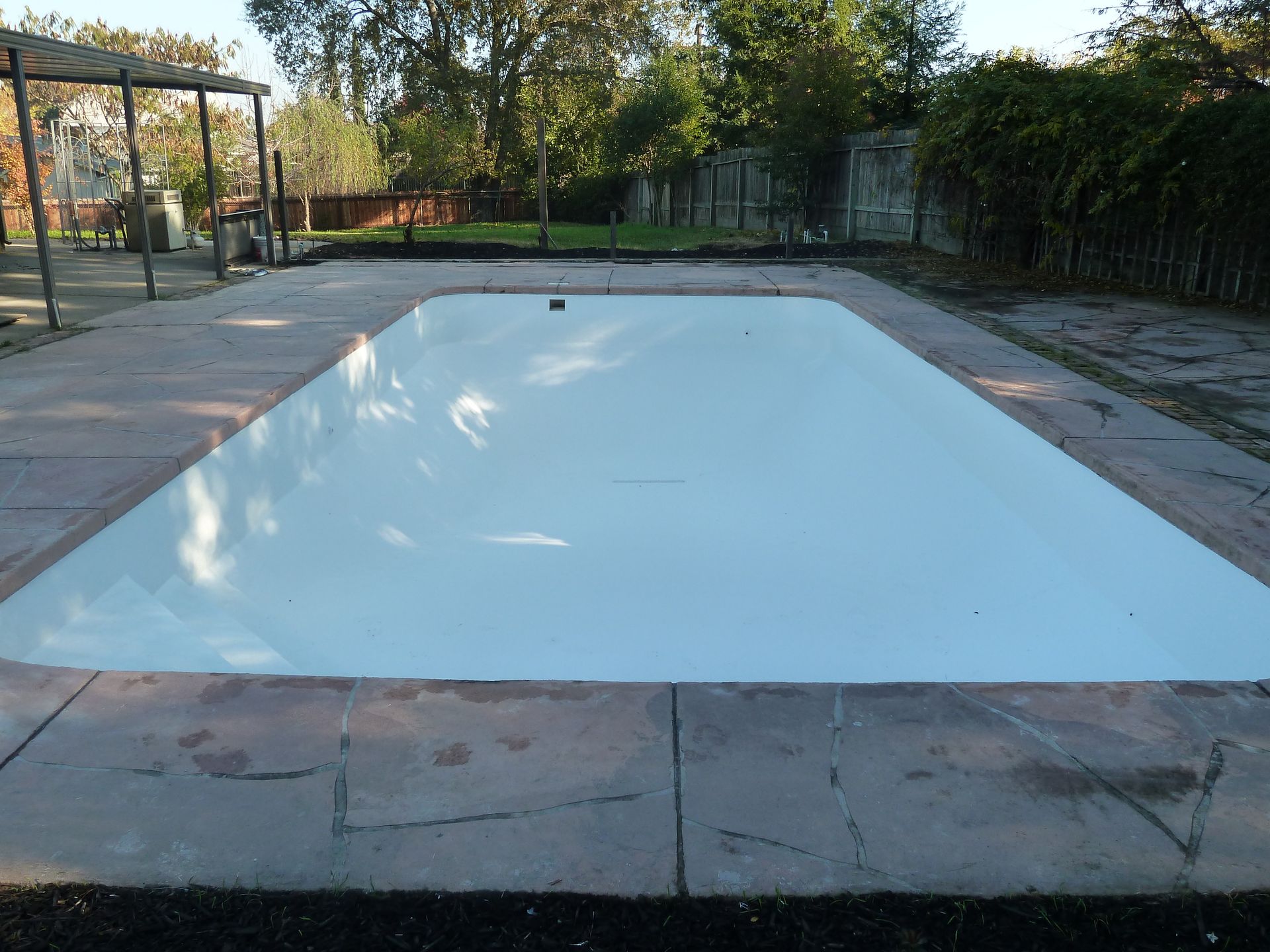 Rectangular pool covered with a white tarp, surrounded by concrete and grass, outdoors. Rectangular pool covered with a white tarp, surrounded by concrete and grass, outdoors.