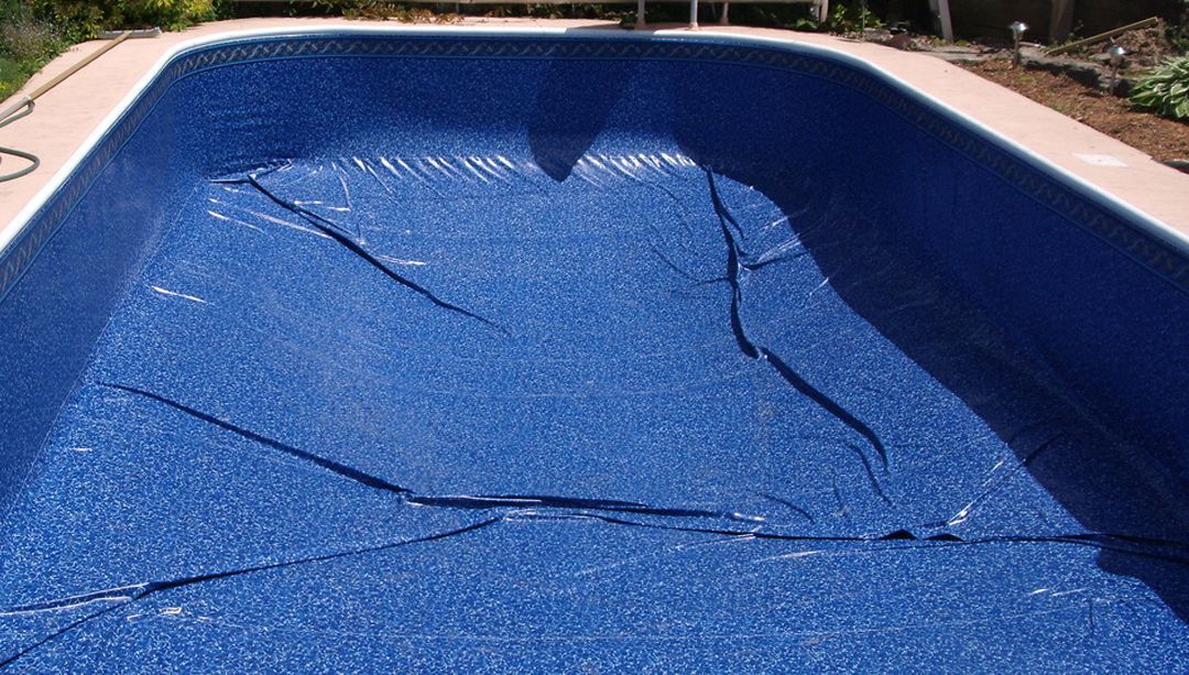 Backyard pool with blue tile interior next to a two-story beige house and patio furniture. Backyard pool with blue tile interior next to a two-story beige house and patio furniture.