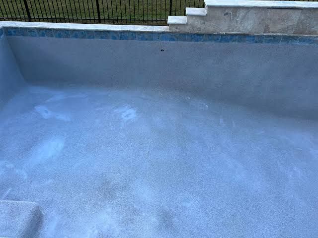 Backyard pool with blue tile interior next to a two-story beige house and patio furniture. Backyard pool with blue tile interior next to a two-story beige house and patio furniture.