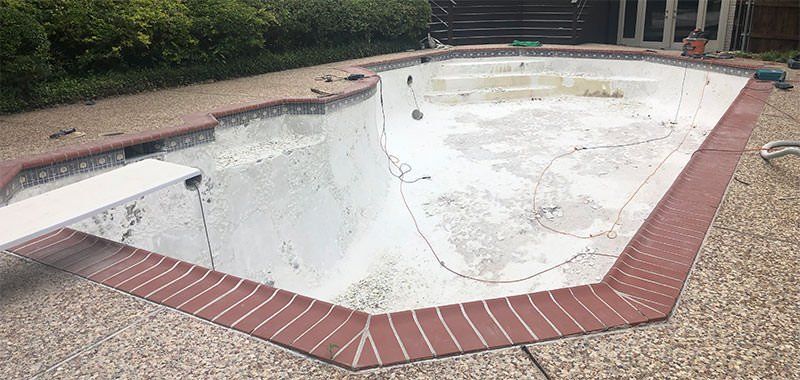 Pool with curved edges, blue water, stainless steel ladder, white coping, and concrete patio. Pool with curved edges, blue water, stainless steel ladder, white coping, and concrete patio.
