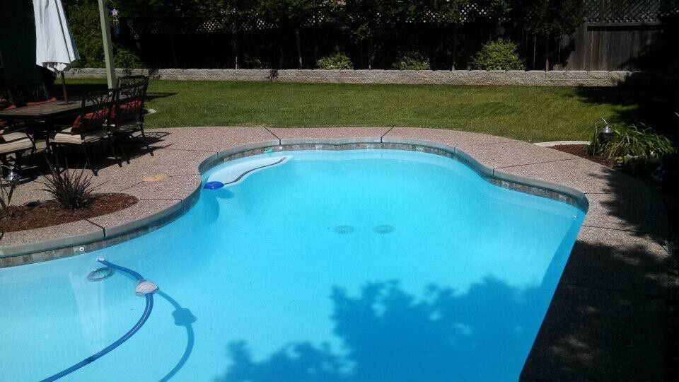 A blue swimming pool with a stone deck, surrounded by green grass and trees. A blue swimming pool with a stone deck, surrounded by green grass and trees.