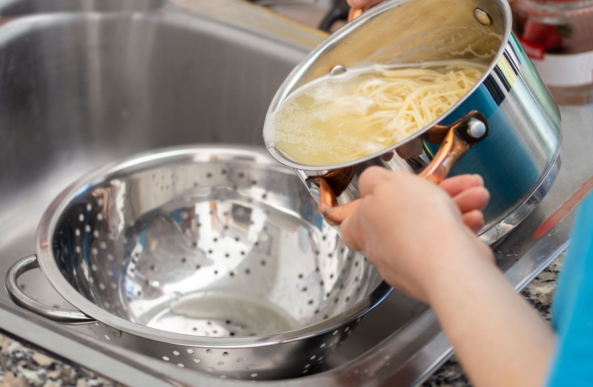 A person is pouring noodles into a strainer in a sink.