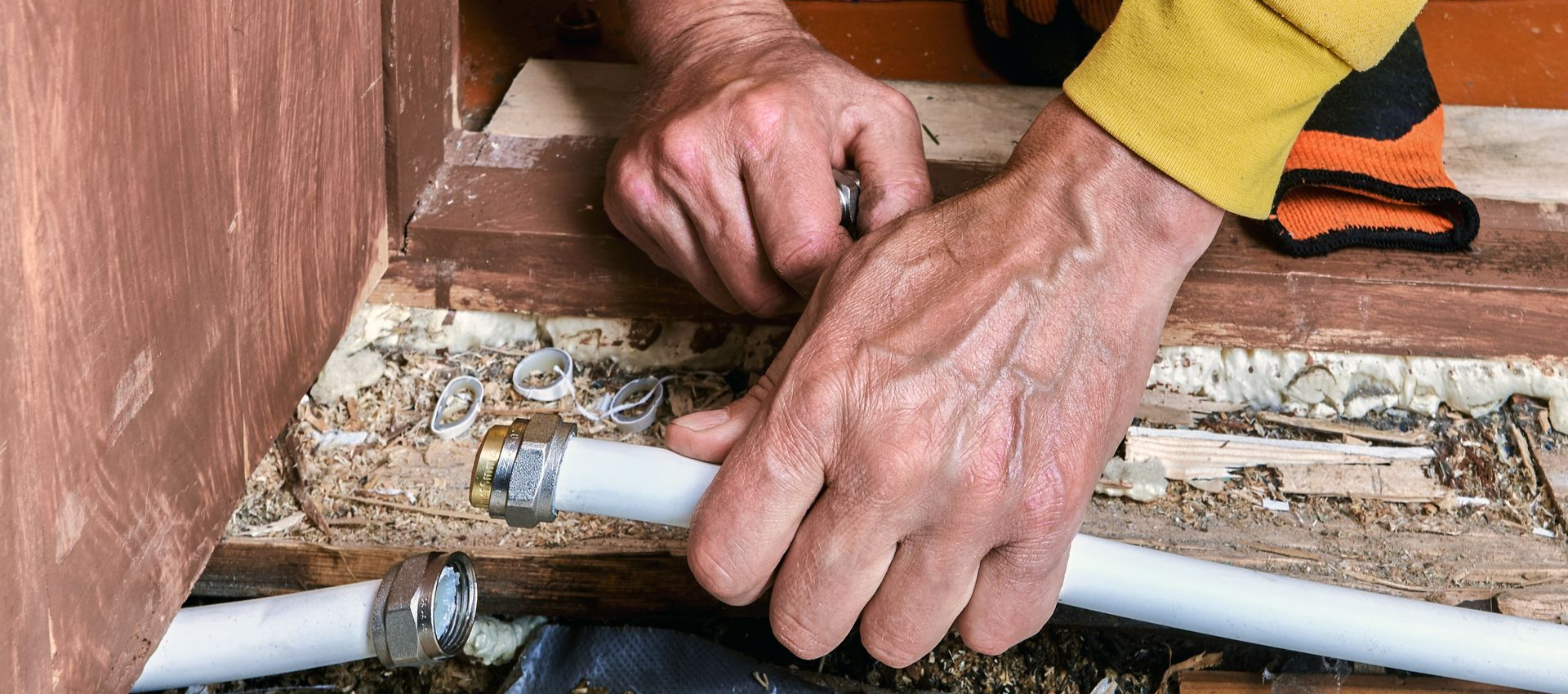 Hands fixing a white pipe, near a wooden door frame, with black and orange sock visible.